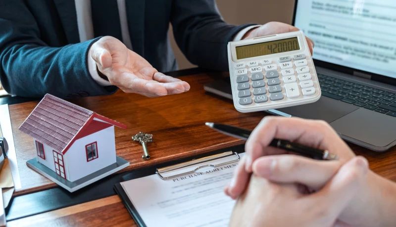 Corretor apresentando os valores da compra com calculadora, chave e miniatura de casa